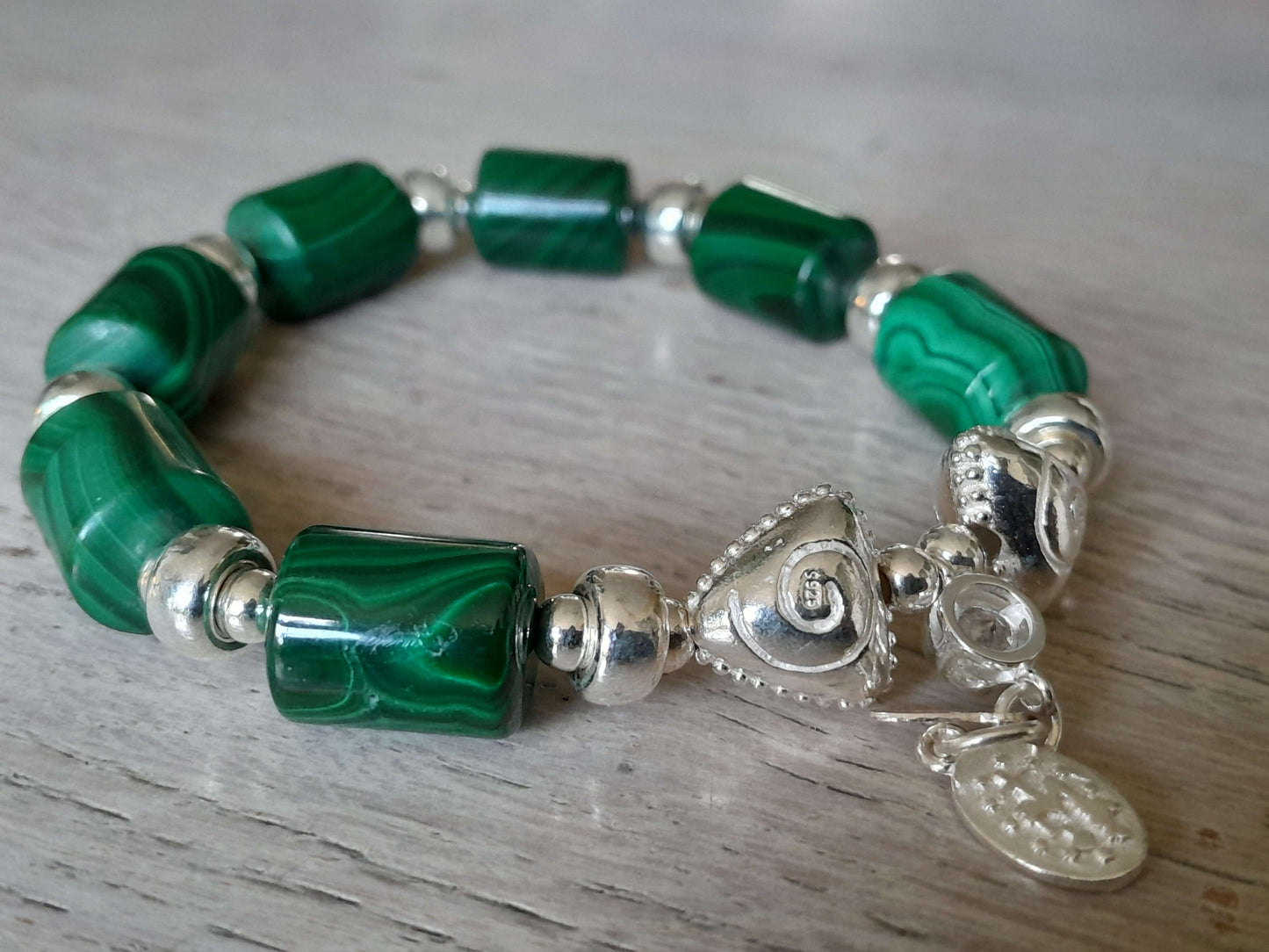 Beautiful malachite bracelet in 925 sterling silver showcasing vibrant green stones and decorative silver charms.