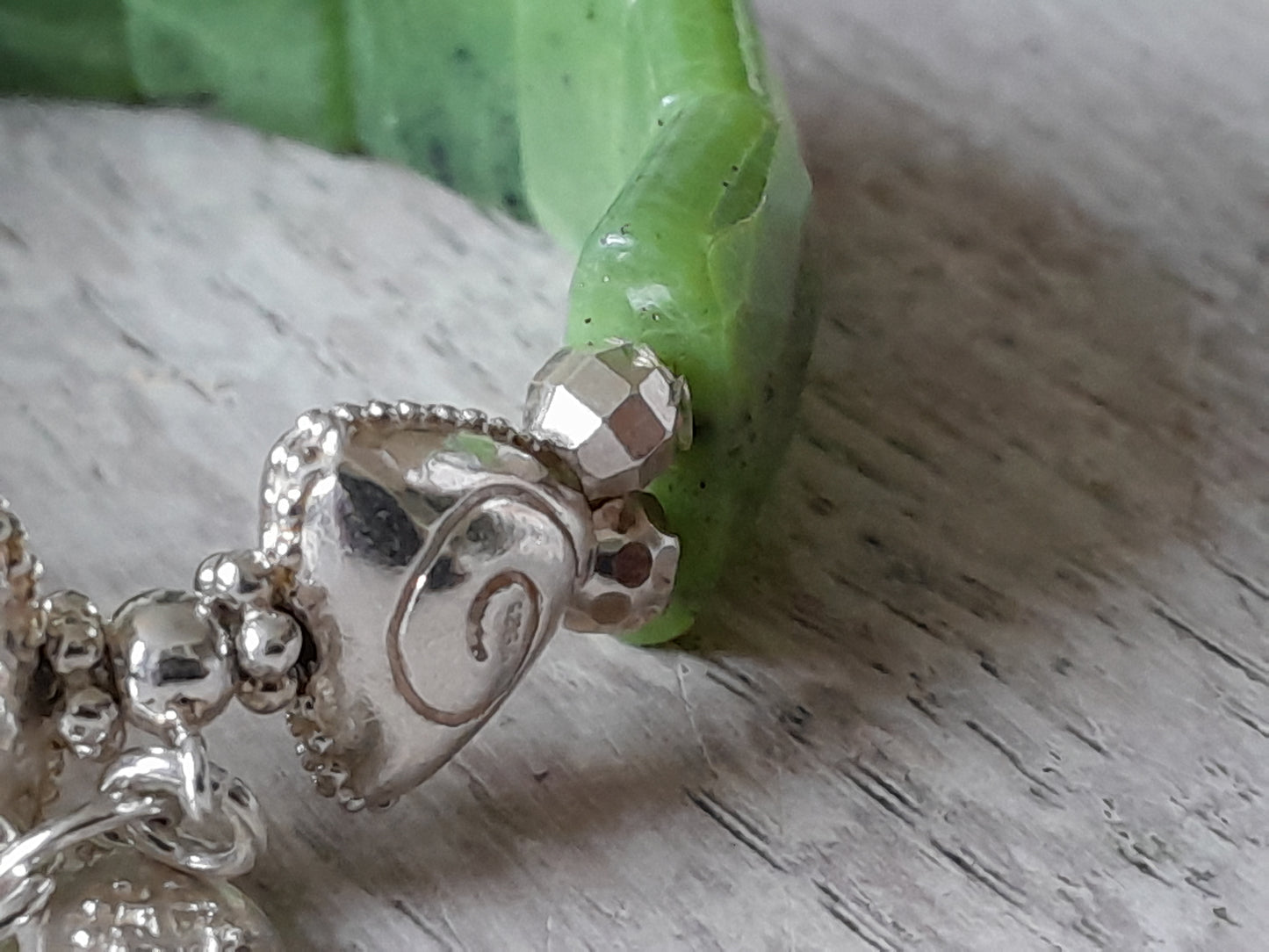 Close-up of nephrite jade bracelet with silver charm and beads showcasing intricate details and vibrant green stones.